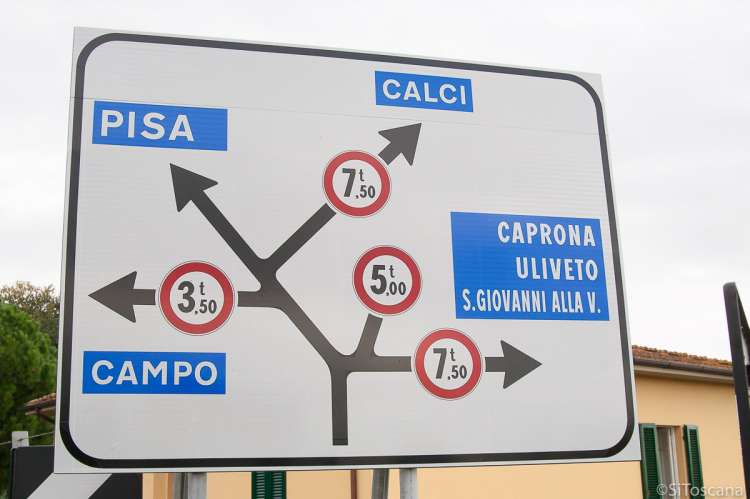 Bildet viser et skilt med veivalg og stedsnavnene Pisa, Calci, Campo, Caprona. Skiltet står ved brua over Arno mellom Zambra og Caprona.