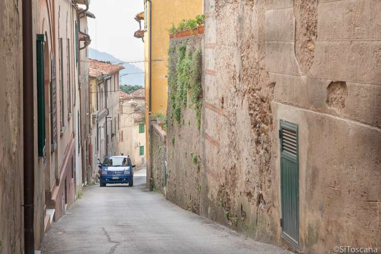 Bildet viser en blå bil som kjører opp hovedgata i middelalderlandsbyen Montemagno. Gata er smal men ikke enveiskjørt. Når to biler møtes må en kjøre inn mot en gateport eller en sidegate. 