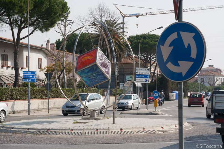 Bildet viser en typisk italiensk rundkjøring med en skulptur i midten. Flere biler er i ferd med å kjøre inn i rundkjøringen. Fremst i bildet vises skiltet for rundkjøring.