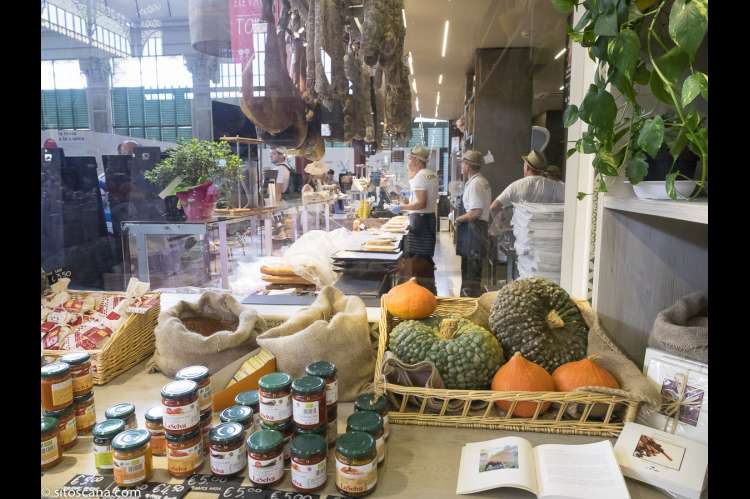 Bildet viser servitører som venter på kunder. Skinker henger ned fra taket. Gresskar ligger utstilt ved disken. I Matmarkedet i Firenze – Mercato Centrale