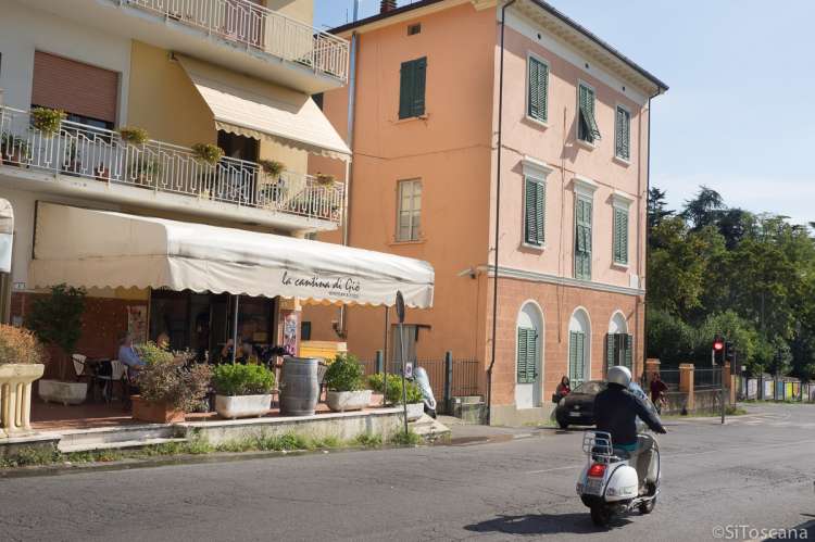 Bildet viser mann som kjører på en scooter mot lyskrysset i landsbyen Calci, ved Pisa i Toscana. På andre siden av gata ligger et spisested med uteservering.