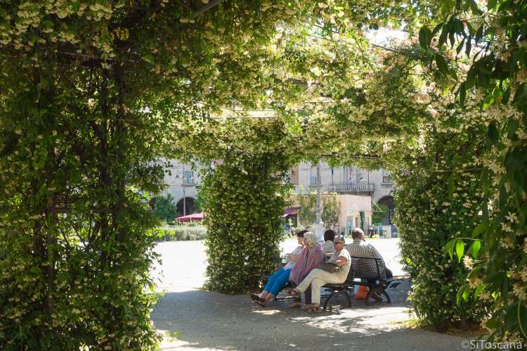 Bildet viser folk som sitter på en benk og hviler seg på Piazza Vittotio Emanuele II, like ved handlegata Corso Italia i Pisa.