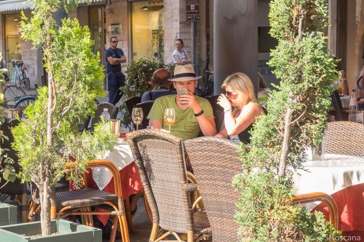 Bildet viser et par som sitter på en fortauskafe i handlegata Borgo Stretti i Pisa. Bildet er tatt en solfylt maidag.