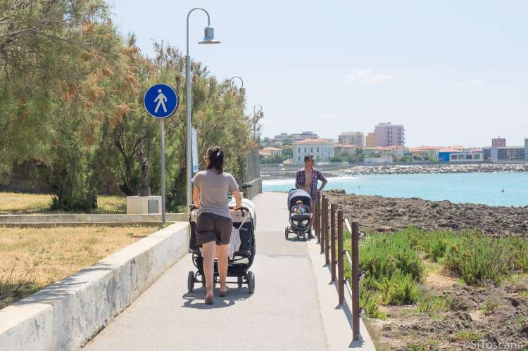 Bildet viser dame med barnevogn på tur langs strandpromenaden i badebyen Castiglioncello.