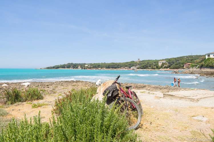 Bildet viser sykkel parkert ved en stein og et par i strandkanten i badebyen Castiglioncello sør for Pisa i Toscana.