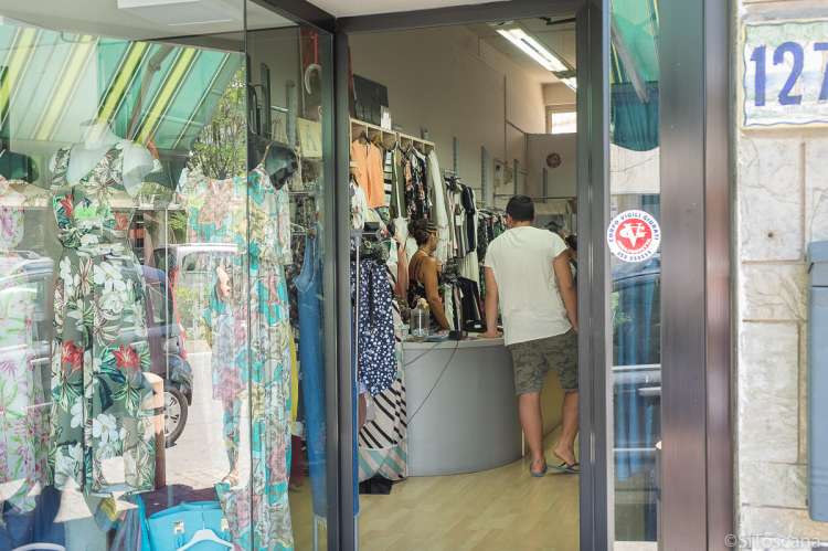 Bildet viser utstillingsvinduet og litt innenfra en av butikkene for dameklær i Tirrenia. En mannlig kunde står ved disken og prater med ekspeditøren.