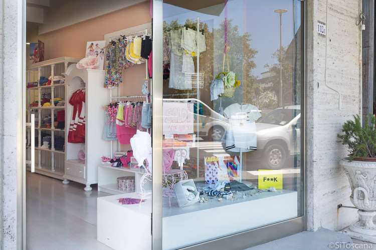 Bildet viser en av butikkene i Tirrenia som selger barneklær. Du ser utstillingsvinduet og litt innover i butikken. Fargerike barneklær henger på veggen og i utstillingsvinduet.