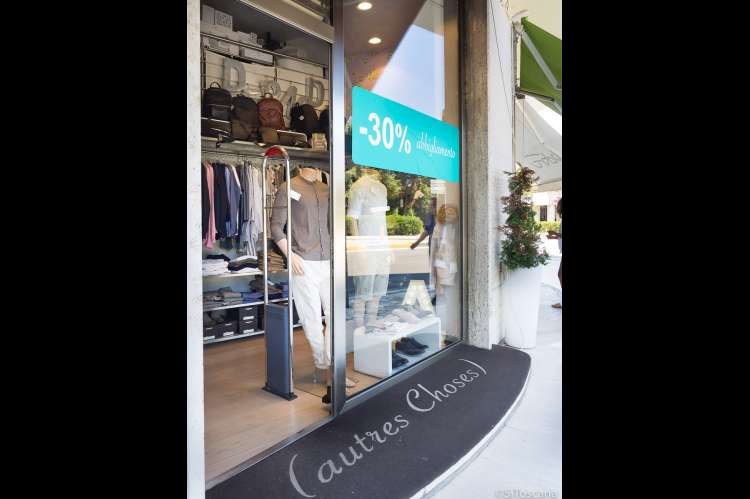 Bildet viser en av butikkene med herreklær. På vinduet henger en turkis plakat som reklamerer for salg. I utstillingsvinduet står det utstillingsdokker med klær. I bakgrunnen, inne i butikken ser du klær som henger og sekker på en hylle.