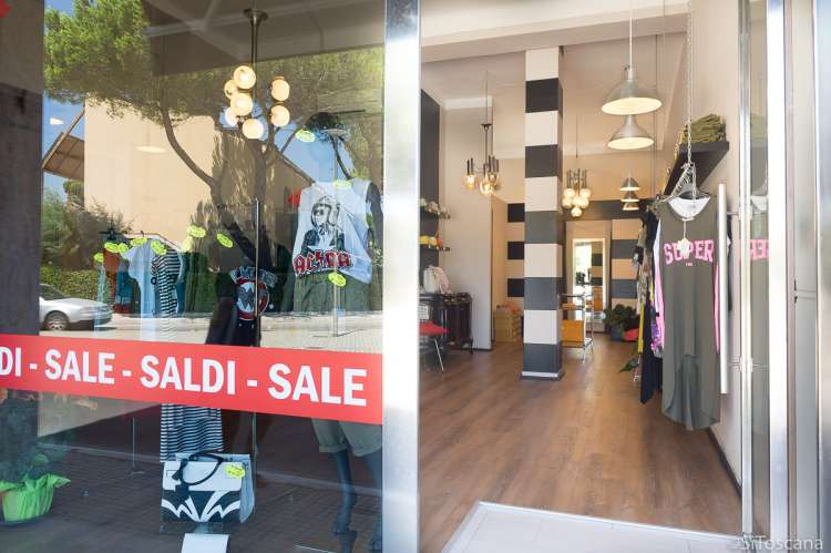 Bildet viser utstillingsvinduet og inngangsdøra til en klesbutikk i Tirrenia. På vinduet henger det rød plakat hvor det er skrevet saldi og sale som betyr salg.