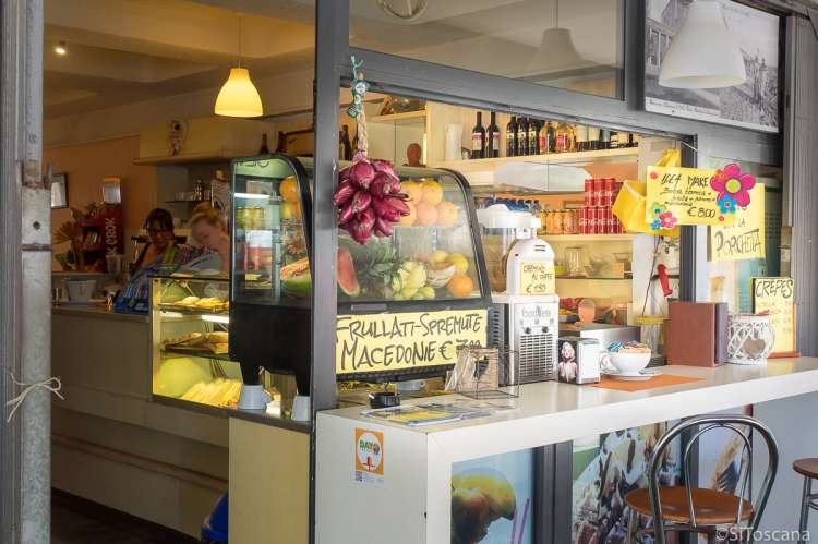 Bildet viser en bar som tilbyr ferskpresset juice, smoothie, fruktsalat med mere. Utenfor er det en bardisk. Innenfor ser du frukt utstilt.