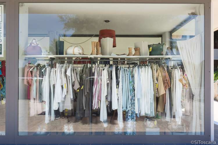 Bildet viser utstillingsvinduet til en av klesbutikkene i Tirrenia. Det henger klær på rekke og rad på ei garderobestang. På ei hylle over står det sko, støvletter og vesker. 