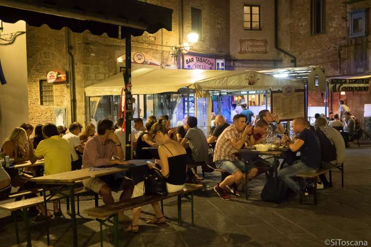 Bildet viser folk som sitter ute på restaurantene på Piazza San Omobono i Pisa en sommerkveld.