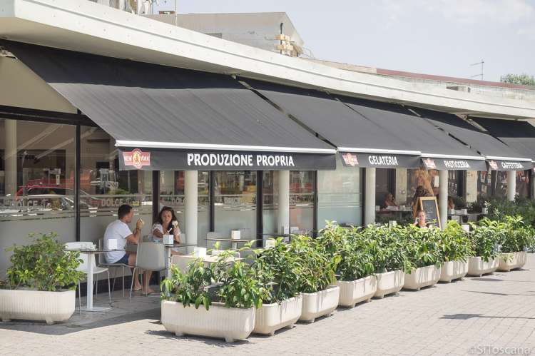 Bildet viser uteserveringen til et av spisestedene i sentrum av Tirrenia. Bordene er omkranset av grønne planter. Et par sitter ved et bord og spiser is.