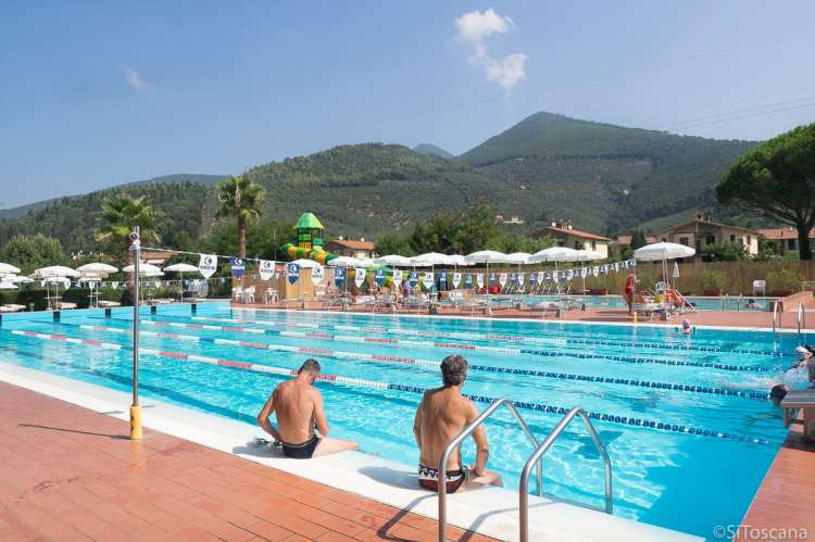 Bildet viser bassenget i La Gabella. To menn slapper av på bassengkanten. I bakgrunnen ser du vannskliene i et annet basseng.