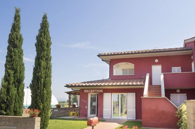 Bildet viser et rødt hus og sypresser. Resepsjonen på Vicino Mare sør i Toscana.