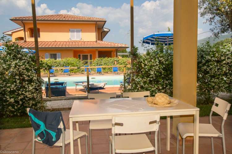 Bildet viser bord og stoler med bassenget bak hekken. Vicino Mare ved kysten sør i Toscana.