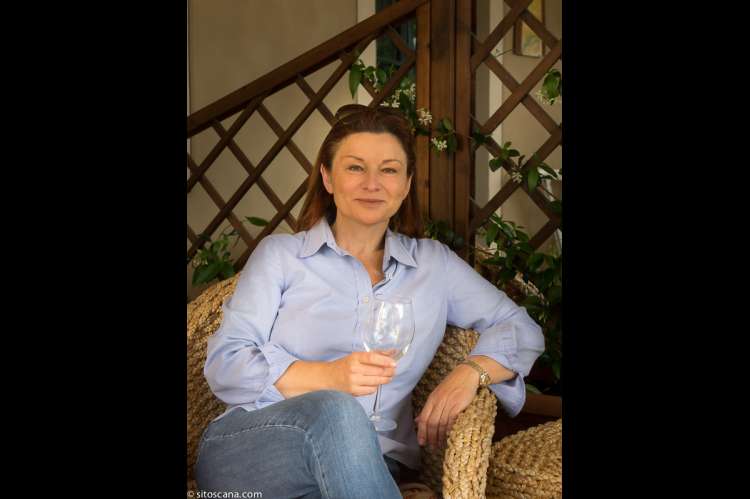 Bildet viser vertinnen Cristiana på terrassen med gårdens vin i glasset., på feriebostedet Girasole, vingård med 10 leiligheter og gangavstand til landsby.