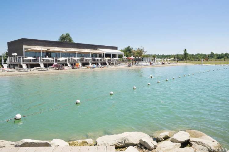 Bildet viser innsjøen Amalia Laghi med sandstrand og restaurant, solsenger og parasoller. Ved Pisa og Pontedera.