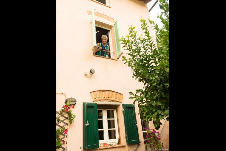 Foto av en gjest som leier ferieleiligheten og nyter utsikten fra vindu utover hus og landskap i landsbyen. 