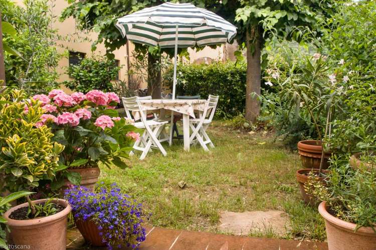 En av hagene ved huset. Frodighet og blomster i terracottakrukker.  Foto.