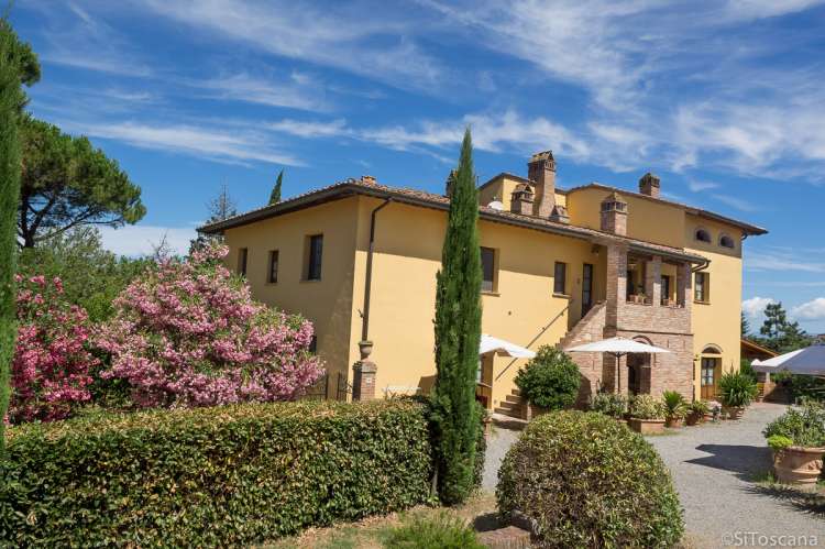 La Bella Lavanderina og Cavallino bak blomsterbusken. Rett frem er Cecco Bilenco og Staccia Buratta. Bilde av det ene feriehuset med ferieleiligheter. Sypress og blomstrende trær.