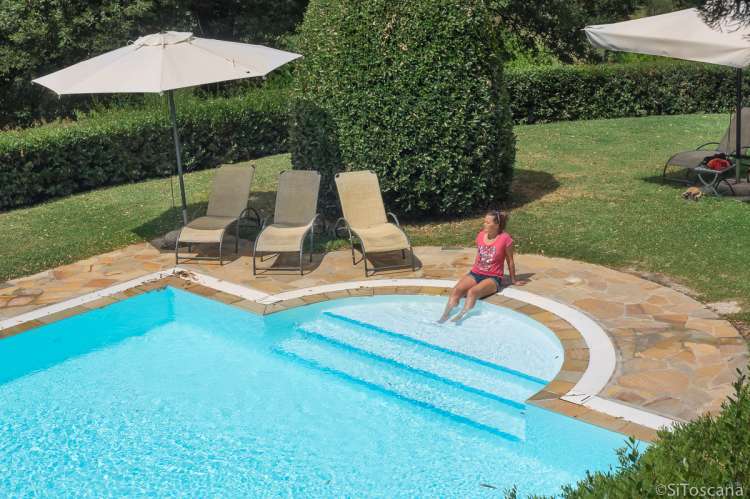 Bassenget på Collina ligger fredelig til i en grønn oase. Bilde av svømmebassenget på vingård i Toscana med solsenger og parasoller.