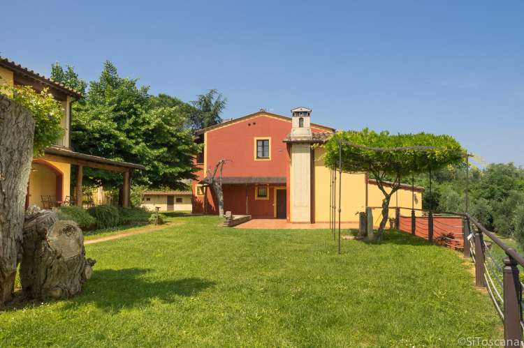 Bildet viser de to husene på feriebostedet La Pergola med plen og en pergola. Ved Pisa i Toscana. 