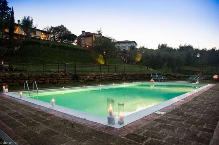 Bildet viser bassenget med levende lys på kanten, i skumringen om kvelden. På feriebostedet La Pergola i Toscana. 