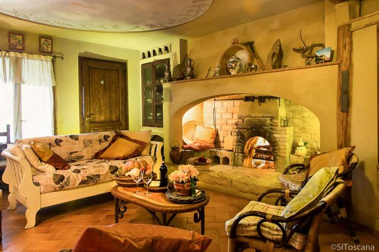 Bildet viser sofa og lenestoler foran peisen inne på restauranten på feriebostedet La Pergola, ved landsby i Toscana.