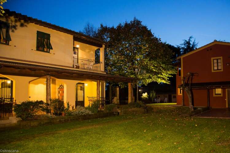 Bildet viser de to husene på La Pergola med plen i mellom. Det er kveld og mørkt. Lys fra mange lamper. På feriebostedet La Pergola, ved landsby i Toscana.