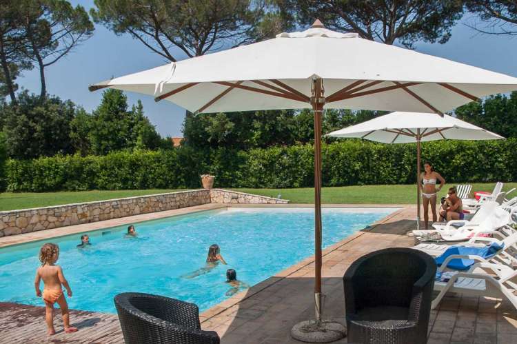 Bildet viser bassenget på Palazzo Gello med solstoler, parasoller og barn som leker. Villa Palazzo Gello ved Pisa i Tocana.