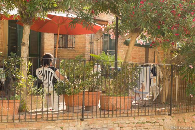 Bildet viser dame under parasoll i en rolig stund utenfor feriehuset Borgo Etruschi i Toscana.