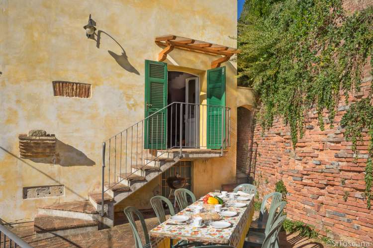 Bildet viser terrasse med spisebord og inngangen til ferieleiligheten Canonica på vingården Borgo Etruschi sentralt i Toscana.