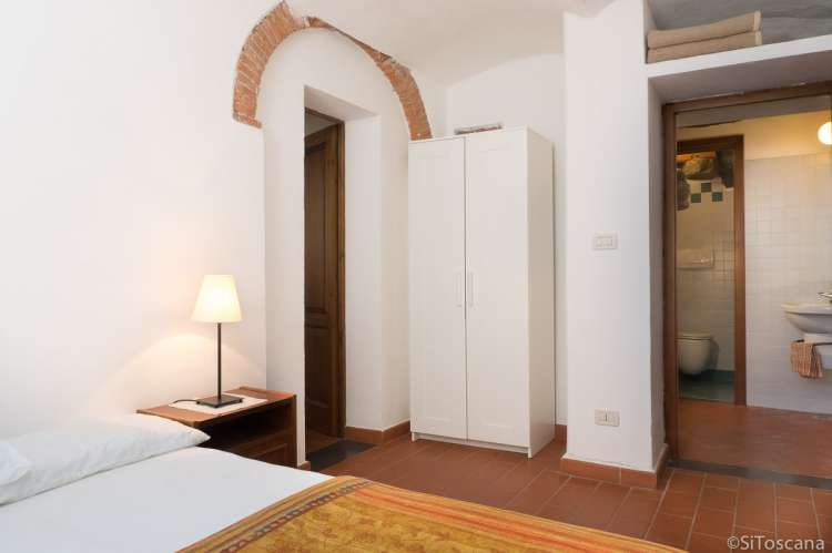 Bildet viser soverom med seng og inngang til baderom i ferieleilighet utenfor Pisa.