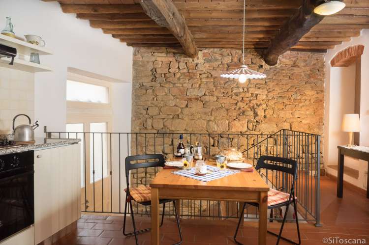 Bildet viser kjøkken med spisesbord og murvegg i ferieleiligheten Karine midt i middelalderlandsby i Toscana.