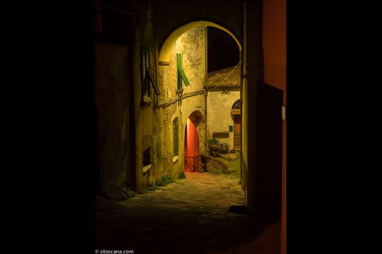 Steinhus med bue over den smale brosteinsgata i Montemagno. Kveldsbilde fra landsbygate. Steinhus med bue over den smale brosteinsgata.