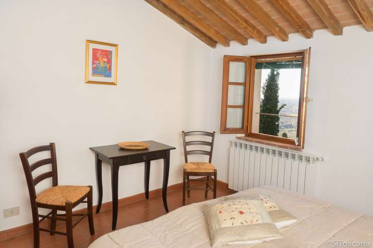 Naboens sypress kan skimtes fra vinduet i 2. etg Naboens sypress kan skimtes fra vinduet i ferieboligen. Soverom med lite bord og stoler. Bilde