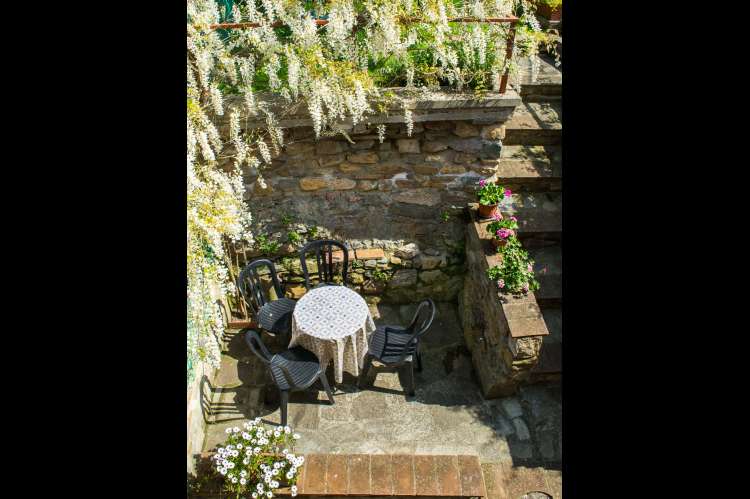Uteplass ved inngangsparti. Hagen er ovenfor. Liten terrasse like ved inngangsdøra. Blomsterflor rammer inn uteplassen. Bilde.