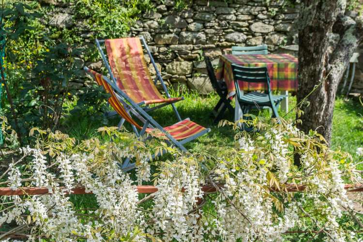 Avslappende omgivelser i egen hage, midt i middelalderlandsby. Vakker blomsterhekk omkranser hagen tidlig på sommeren. Solstoler og spisebord. Bilde.