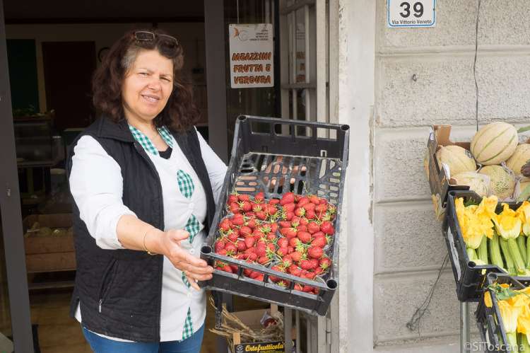 Bildet viser dame med jordbær utenfor matbutikk i landsby nært Pisa.