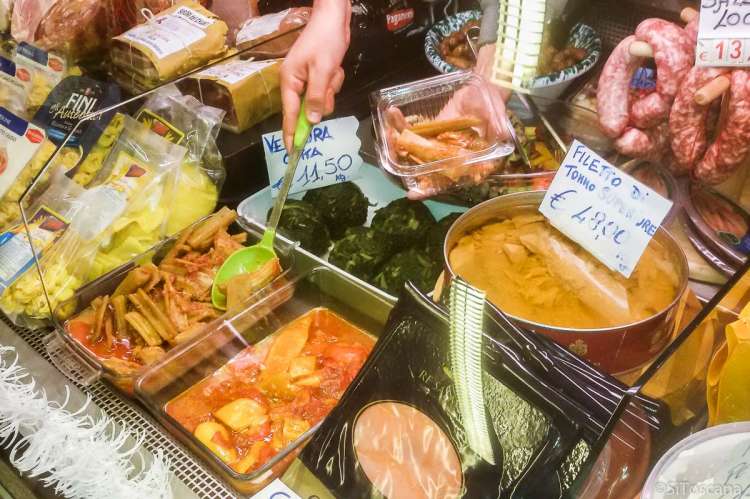 Bildet viser hånda til en ekspeditør som tar opp delikatesser med en øse i en disk i en matbutikk i landsbyen Calci.