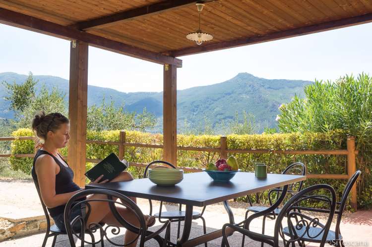 Bildet viser terrasse og dame som leser bok utenfor ferieboligen Villa Vista i Toscana.
