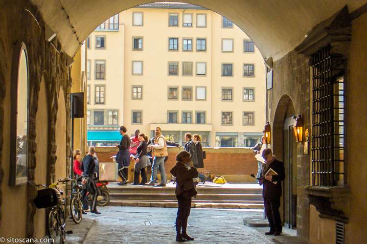 Bildet viser mennesker som sitter og går i en buegang i Firenze sentrum. I Toscana, i Italia.