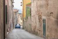 Bildet viser en blå bil som kjører opp hovedgata i middelalderlandsbyen Montemagno. Gata er smal men ikke enveiskjørt. Når to biler møtes må en kjøre inn mot en gateport eller en sidegate. 