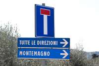 Bildet viser tre skilt. Ett med blindgate. Ett med pil i retning stedet Montemagno. Ett skilt med pil og tekst på italiensk: Tutte le direzioni som betyr Alle retninger.