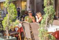 Bildet viser et par som sitter på en fortauskafe i handlegata Borgo Stretti i Pisa. Bildet er tatt en solfylt maidag.