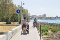 Bildet viser en mann med barnevogn og en kvinne med barnevogn som spaserer på strandpromenaden i Castiglioncello i Toscana en solfylt dag i juni.