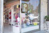 Bildet viser en av butikkene i Tirrenia som selger barneklær. Du ser utstillingsvinduet og litt innover i butikken. Fargerike barneklær henger på veggen og i utstillingsvinduet.