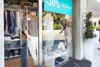 Bildet viser en av butikkene med herreklær. På vinduet henger en turkis plakat som reklamerer for salg. I utstillingsvinduet står det utstillingsdokker med klær. I bakgrunnen, inne i butikken ser du klær som henger og sekker på en hylle.