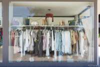 Bildet viser utstillingsvinduet til en av klesbutikkene i Tirrenia. Det henger klær på rekke og rad på ei garderobestang. På ei hylle over står det sko, støvletter og vesker. 